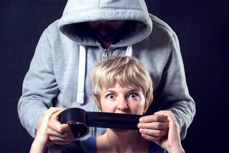 Man in hooded sweater covering a woman'smouth with scotch tape. Concept of violence or kidnapping.